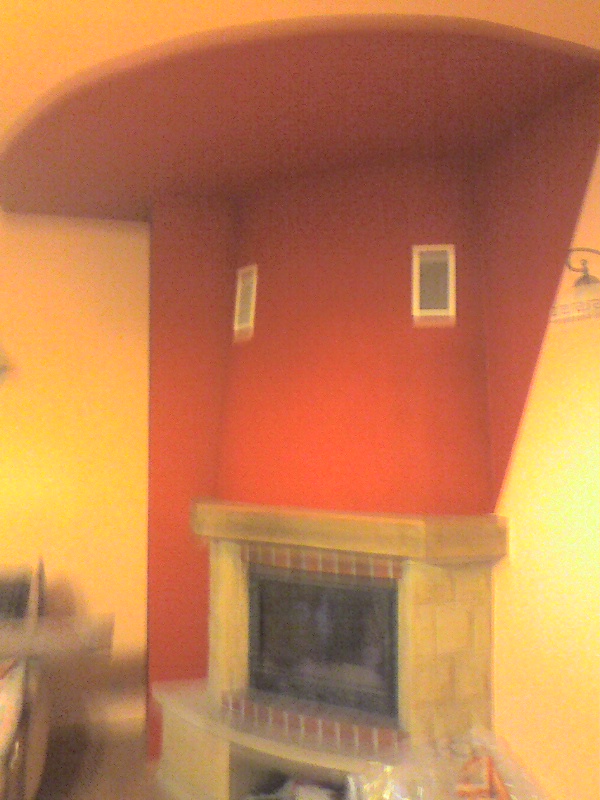 Czerwona ściana z kominkiem i dwoma małymi obrazkami, widok z dołu, po remoncie, z elementami zabezpieczającymi z folii.